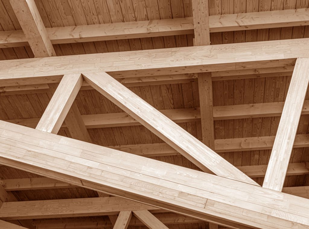 Vue intérieure d'une charpente en bois. On peut observer des fermes en bois triangulaires et des chevrons plus fins.