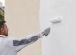 Artisan appliquant une sous-couche façade au rouleau sur un mur extérieur avant peinture